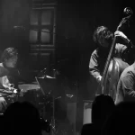 a black and white photo of musicians on stage, there's a drumkit, a double bass and a piano