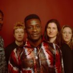 Jarabi Band, there are 6 members looking at camera and a red background
