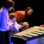 kids and some adults look curiously at a xylophone
